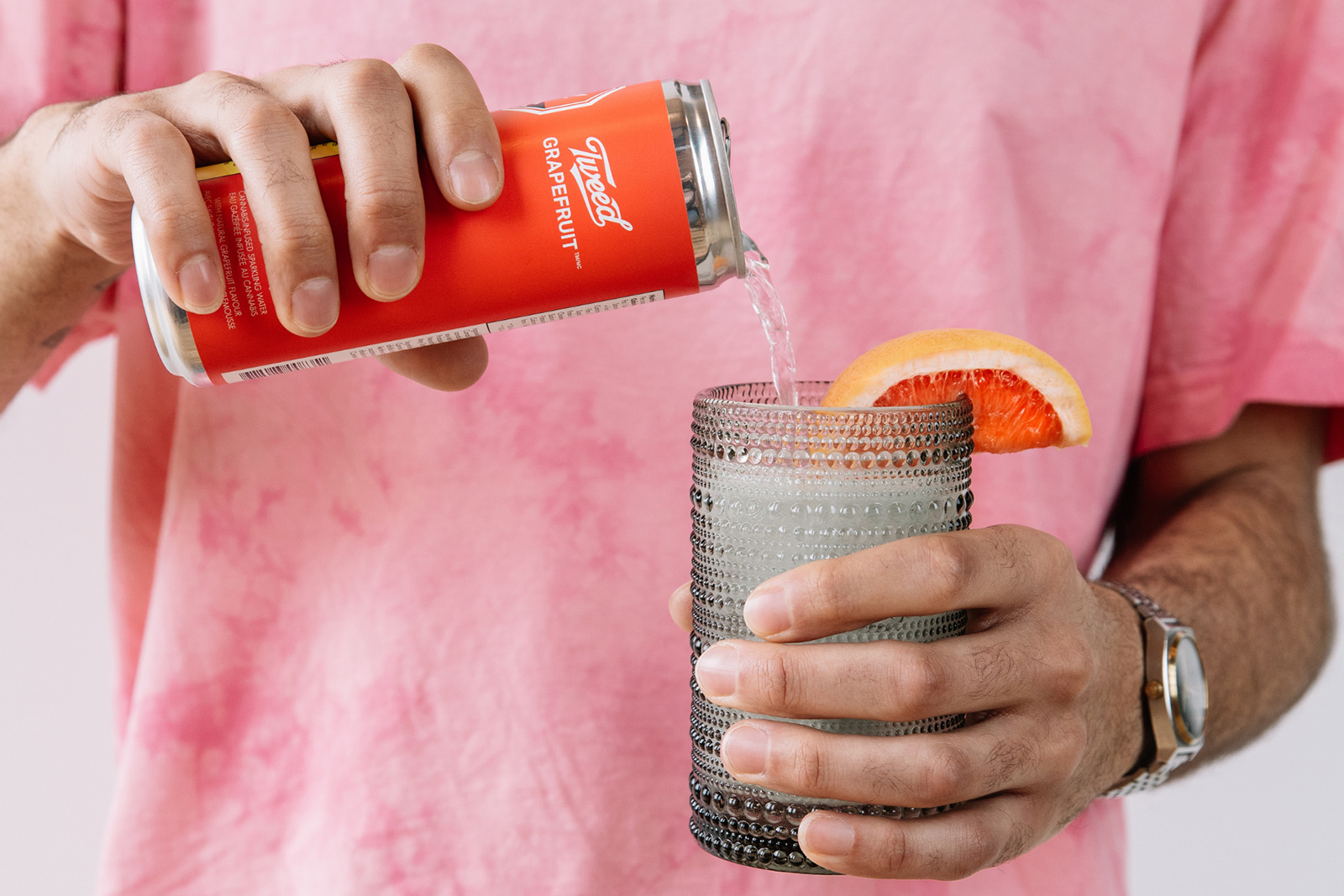 a person in a pink shirt pours a Tweed Grapefruit drink into a glass