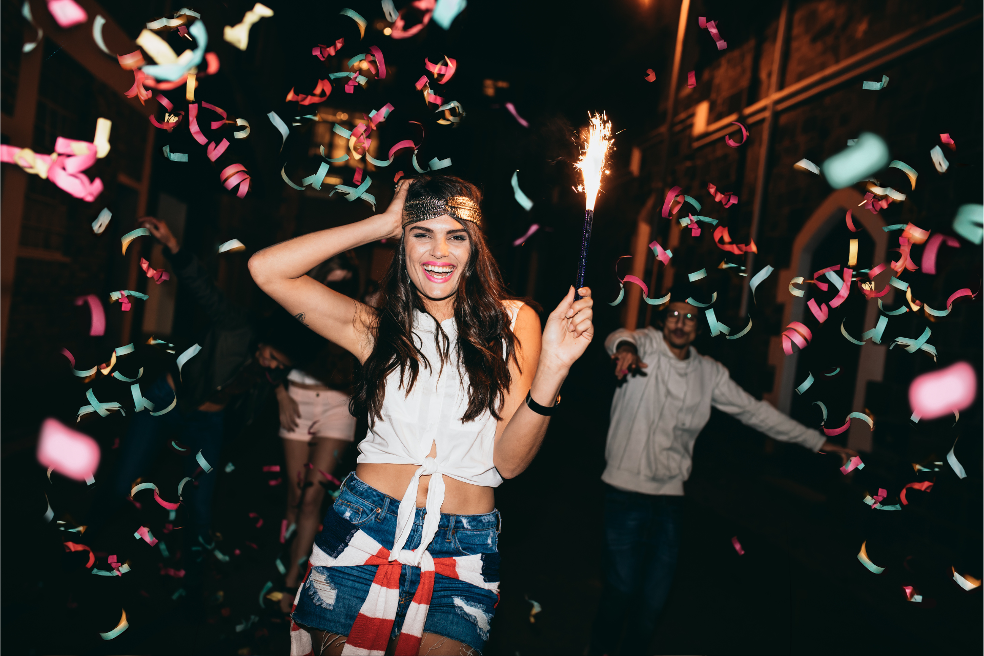 a woman holding a sparkler at a birthday party outside smiling at the camera
