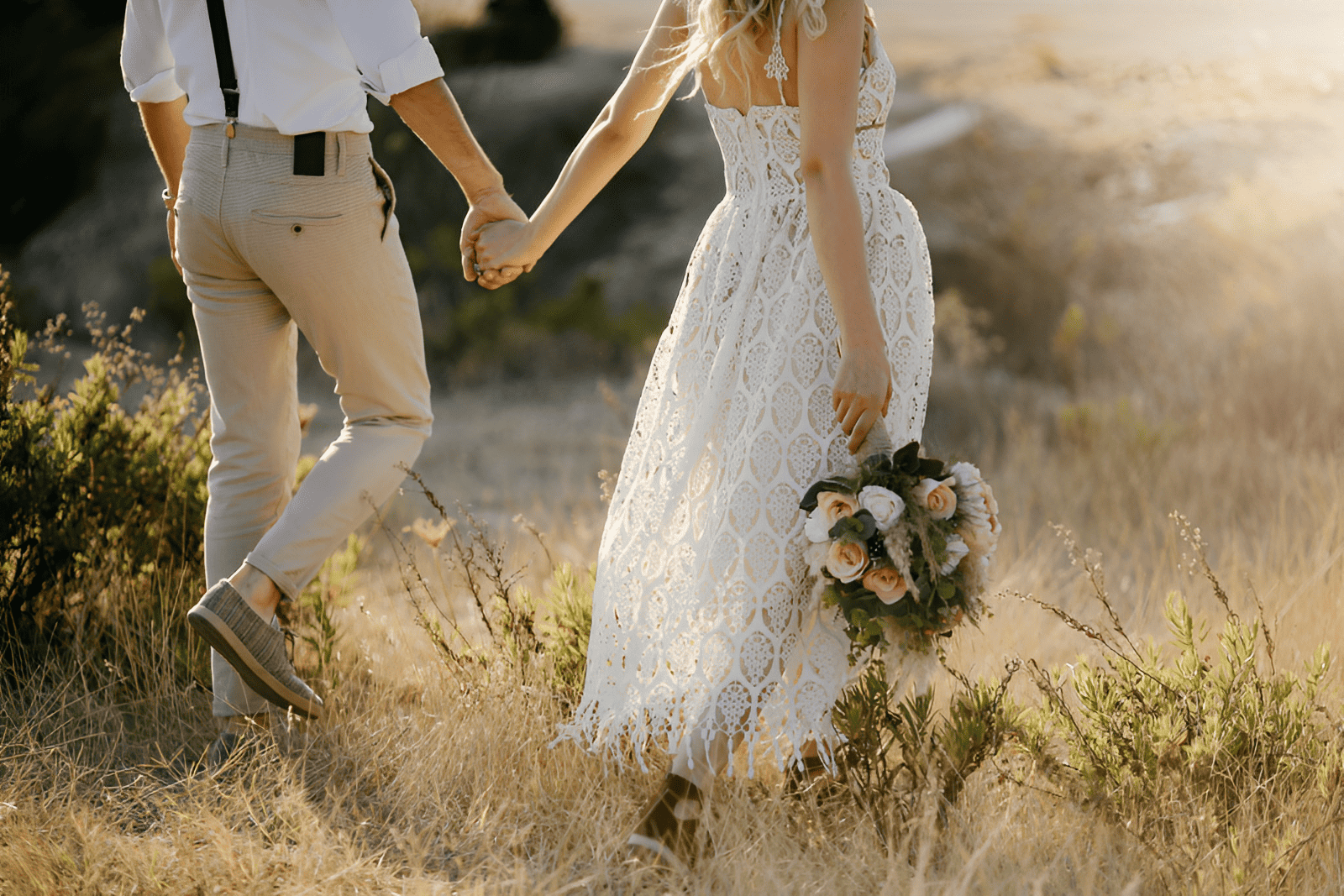 A bride and groom holding hands while walking through a field