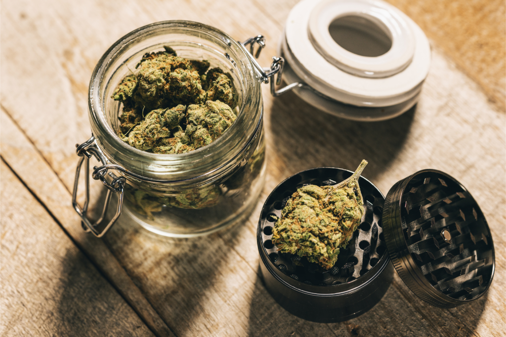  a container of cannabis with a large bud placed on an open grinder
