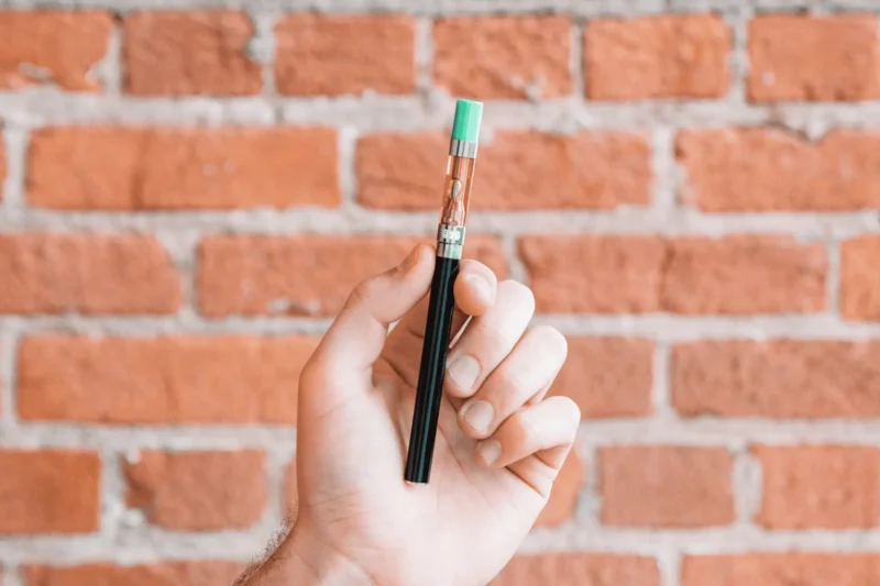 A hand holding a disposable vape pen against a brick wall background