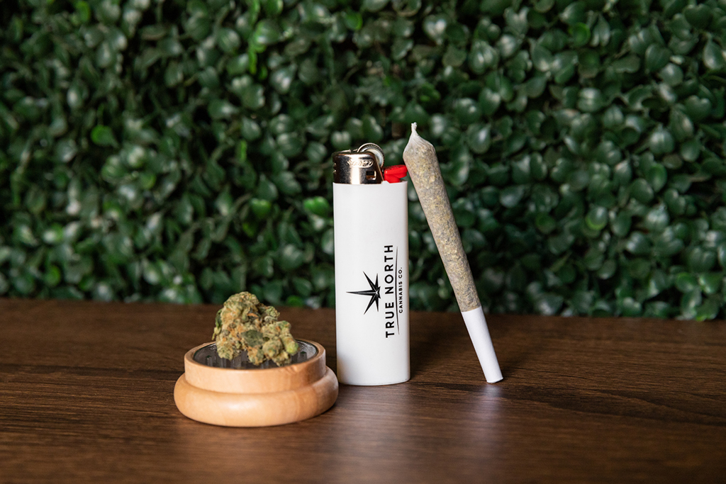 A True North Cannabis Co. flower, roll, and lighter on a wooden table