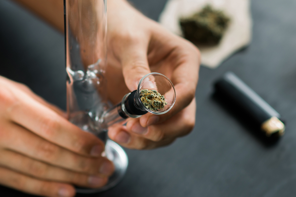 A person fixing a bowl with ground weed on the bong downstem