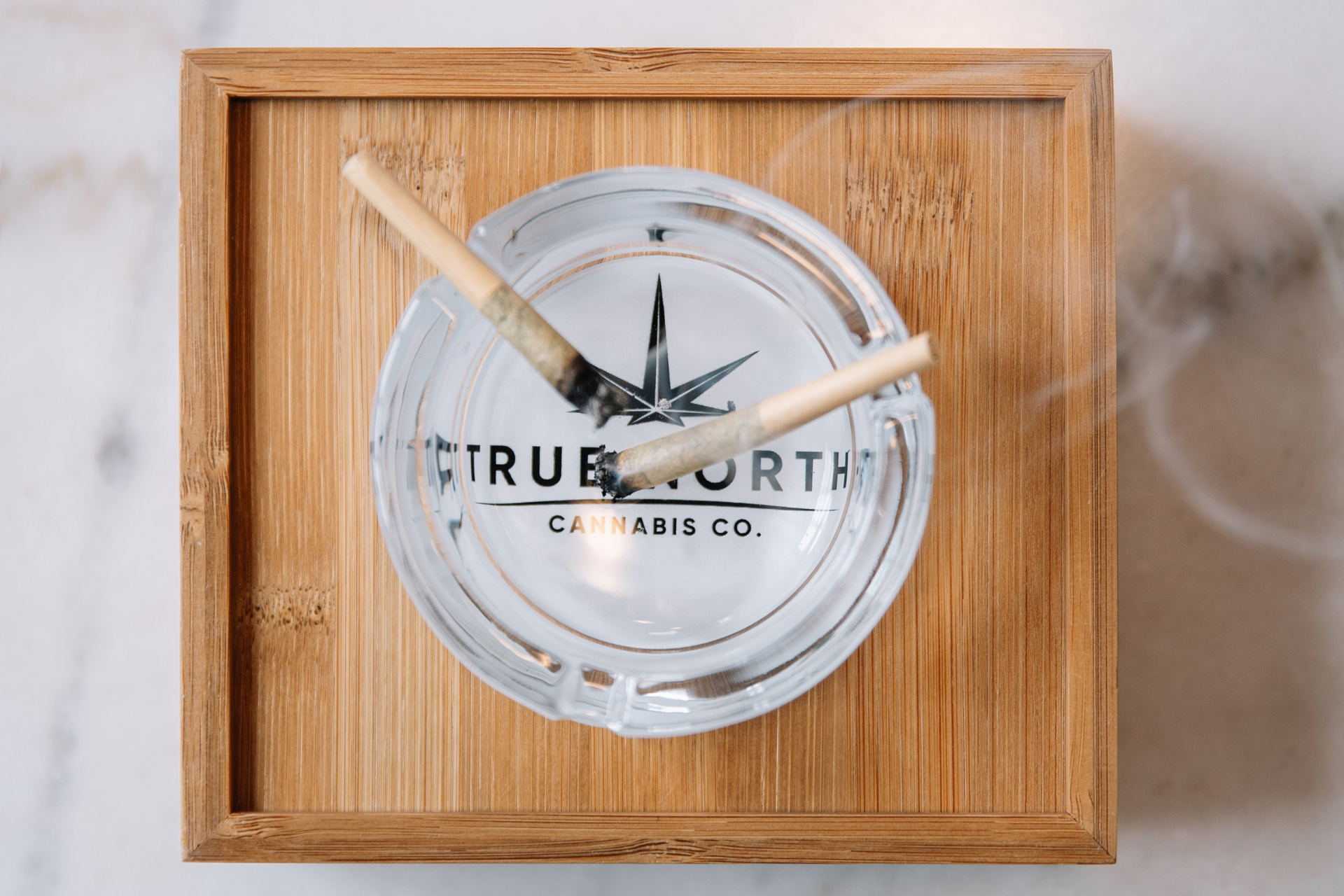 Two lit pre-rolls on a glass ashtray from True North Cannabis Co.