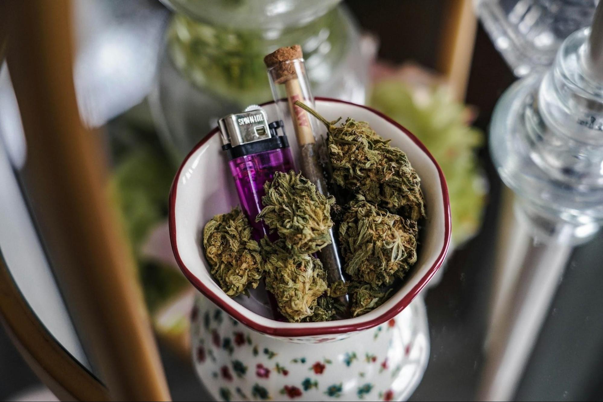 A pre-roll joint nestled between a cup of cannabis flower and a lighter
