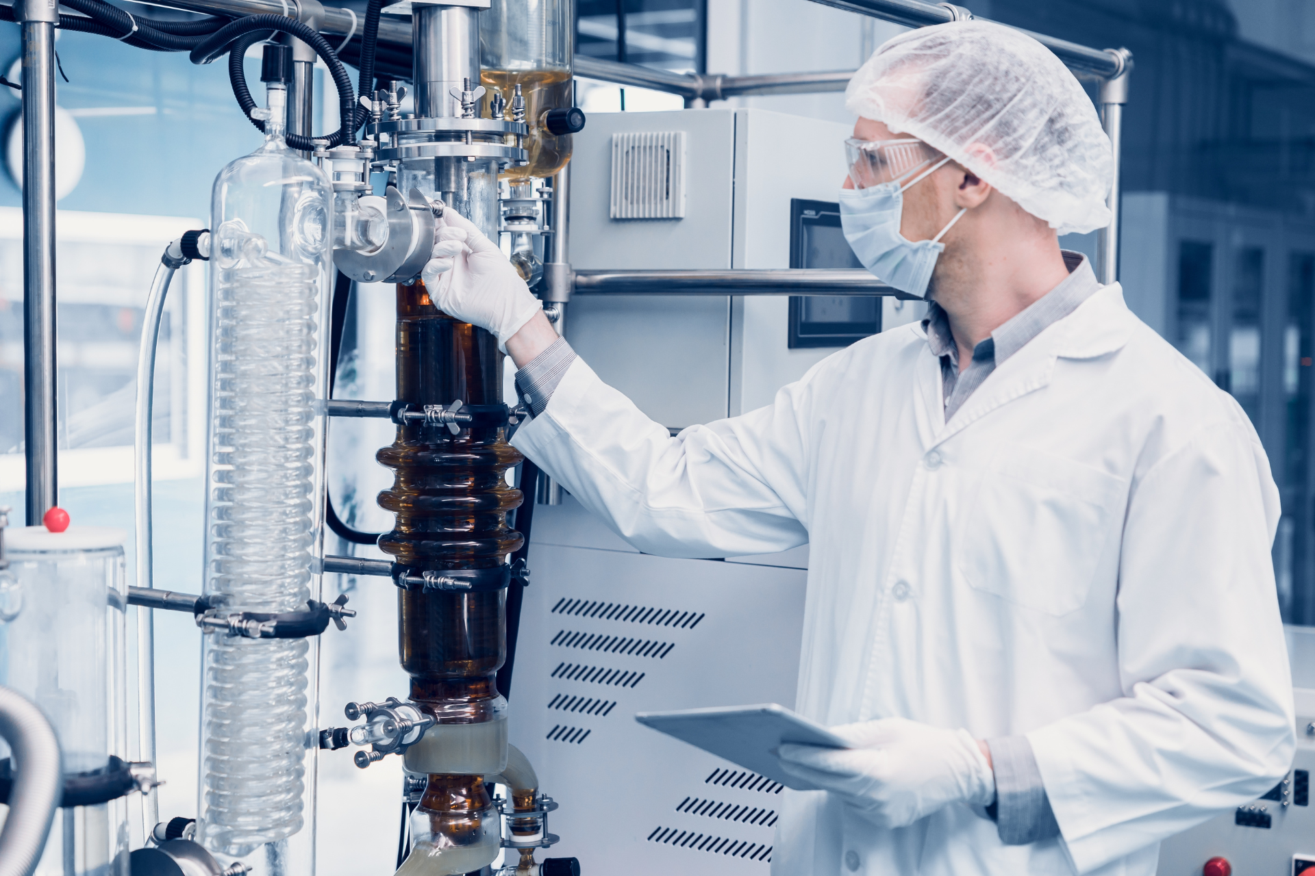 A scientist wearing a labcoat, goggles, hairnet, mask, and gloves using an extraction machine in a lab