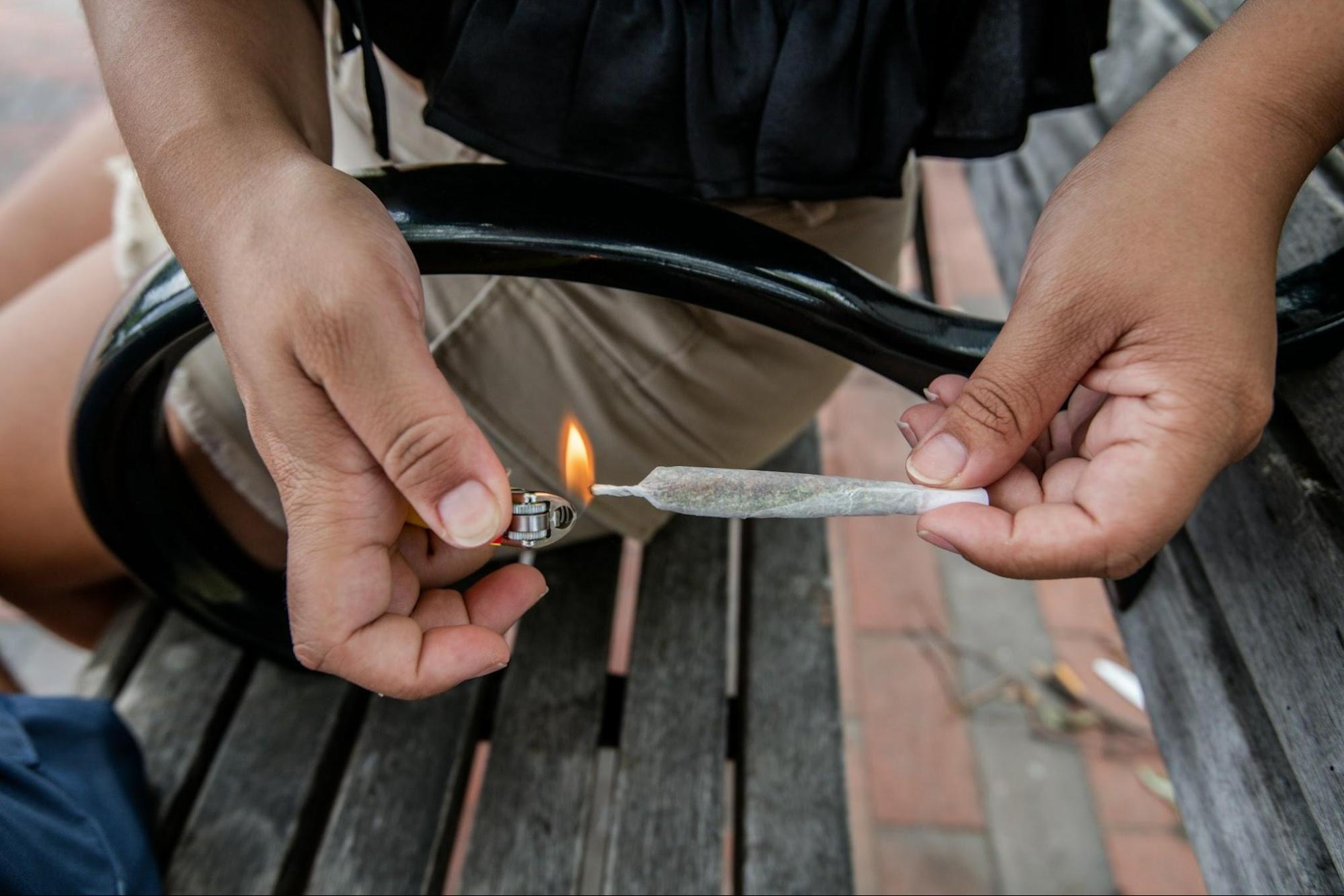 A person on a bench, lighting a joint