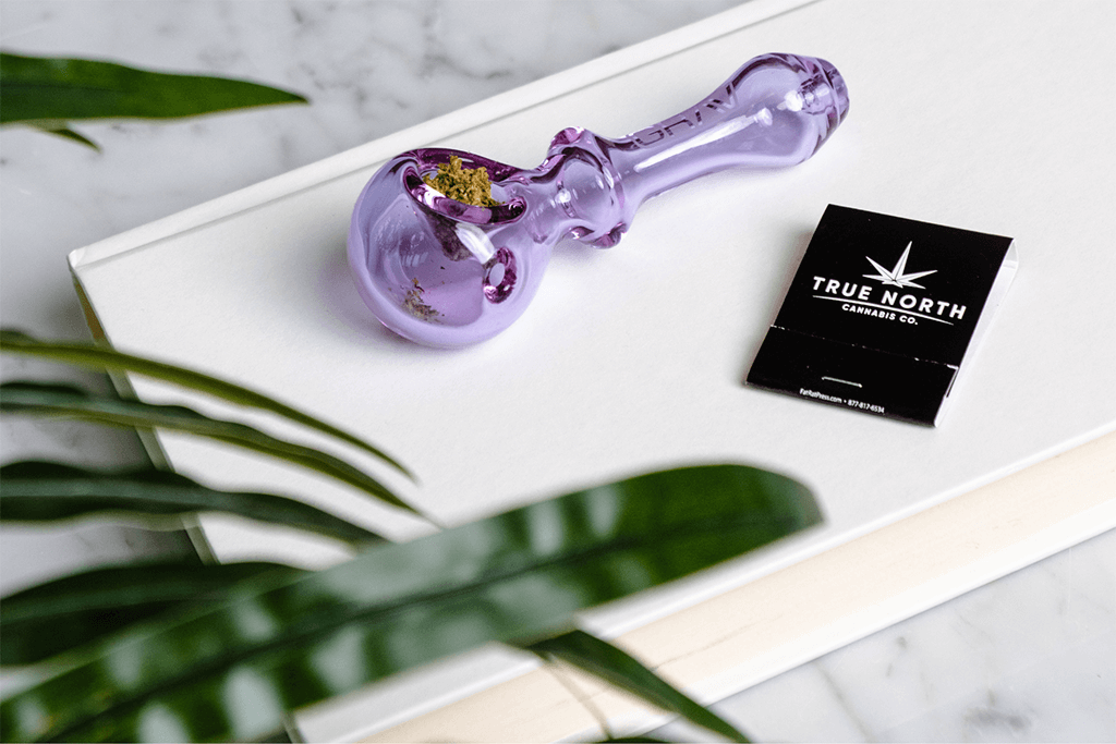  Cannabis packed in a purple pipe next to a True North Cannabis Co. matchbook 