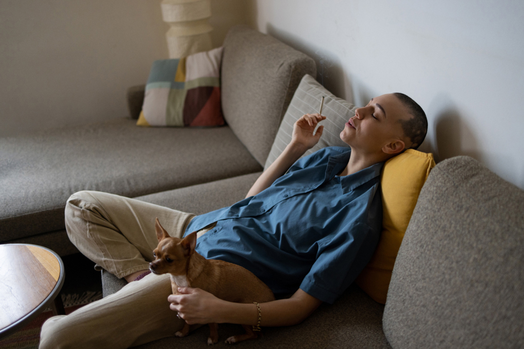 a person unwinding and smoking a pre-roll with their eyes closed on the couch 
