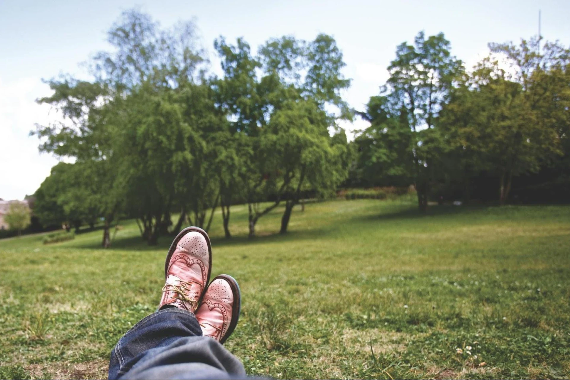 Person lying on grass in a field surrounded by trees under a partly cloudy sky
