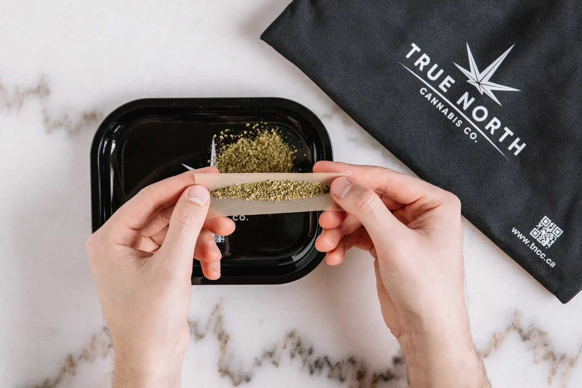 A person rolling a joint on a True North Cannabis Co. branded rolling tray